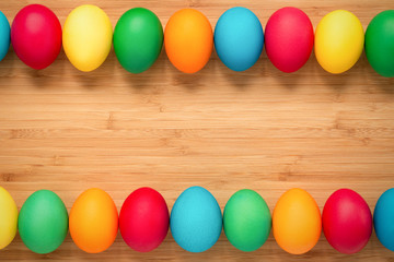 Multicolored easter eggs on a light wooden background. Eggs on top and bottom in a row. The concept of a holiday and a happy Easter. Place for text