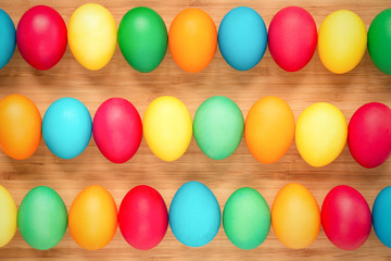 Multicolored easter eggs on a light wooden background. Eggs in three rows. The concept of a holiday and a happy Easter.