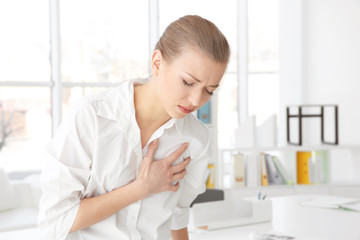 Heart attack concept. Young woman suffering from chest pain in office