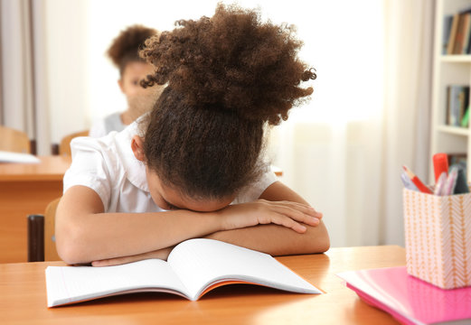 Portrait of tired African elementary schoolgirl sitting in classroom