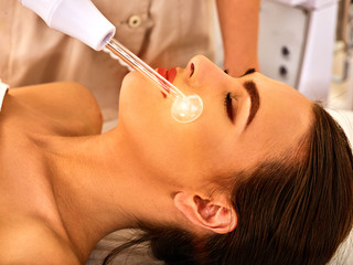 High frequency machine in spa salon. Young woman receiving electric darsonval facial massage after procedure at beauty room close up.