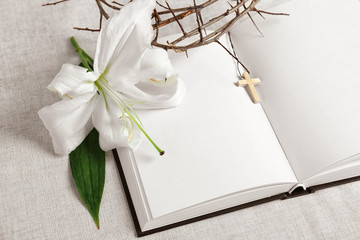 Blank opened book, lily and crown of thorns on white fabric background