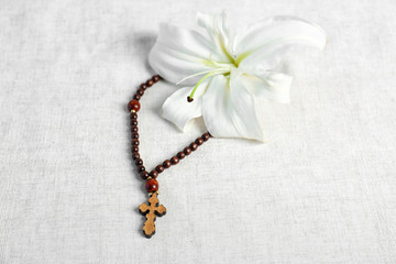 Fototapeta na wymiar White lily and rosary on light fabric background