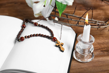 Opened blank book, candle with holder, rosary and crown of thorns on wooden table