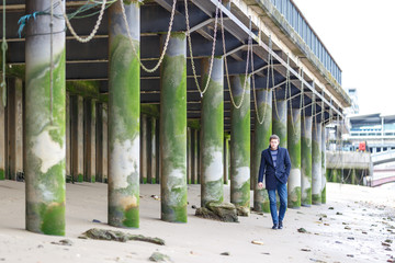 Man portrait at low tides of Thames with green stilts