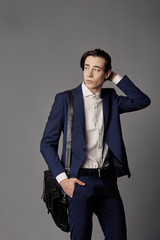 Business fashion man wearing blue suit with white shirt and bag on his shoulder. Studio shot against grey