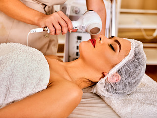 Ultrasonic facial treatment ultrasound face machine. Woman wearing medical hat receiving electric lift massage spa salon. Electronic stimulation female muscles. Skin care microcurrent therapy .