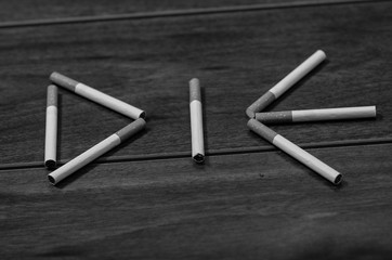Cigarettes lying on wooden surface shaped into the word die, artistic anti smoking concept, black and white edition