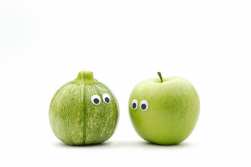 vegetables against fruit - zucchini and green apple with googly eyes on white background