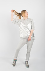 Young hipster girl wearing grey clothes and sneakers posing isolated on white background. She is holding hair up