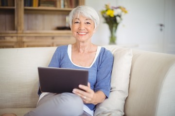 Smiling senior woman using digital tablet in living room - Powered by Adobe