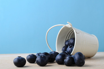 Bucket of Blueberries Spilling on to Wooden Table with Light Blue Background