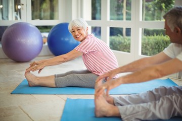 Senior couple performing stretching exercise on exercise mat