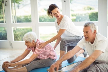 Female trainer assisting senior couple in performing exercise - Powered by Adobe