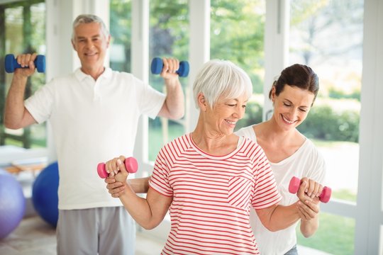 Female trainer assisting senior couple in performing exercise