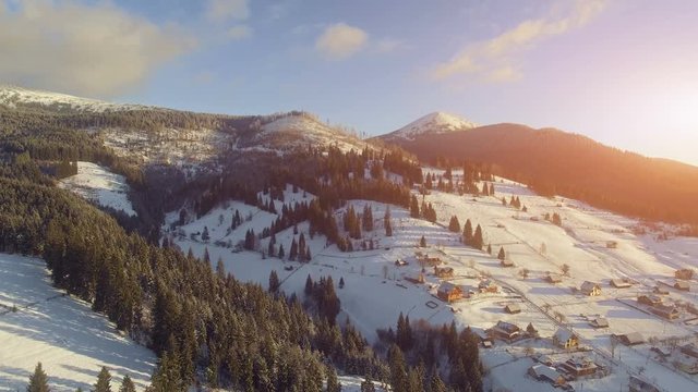 4K Aerial Drone View: Flight over Ski resort in winter, sunset time. Houses and hotels along the road. Pine tree forest around. Majestic nature landscape. Bukovel, Carpathian Mountains, Ukraine