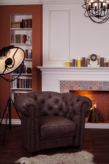 Black art lamp tripod near luxury brown leather chair at modern fireplace background. Home library interior design. Vertical