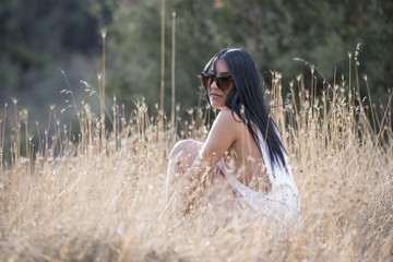 Young slim woman pose outdoor wear a tanktop shirt sitting on the dry grass © Domforstock