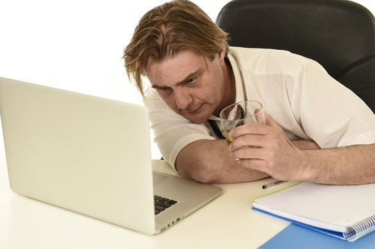 wasted messy alcoholic businessman drinking whiskey working at laptop computer desk at office