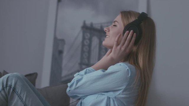 Young Caucasian teen girl putting on headphones on a sofa at home and enjoying music from a vinyl turntable. 60FPS SLO MO 4K UHD RAW edited footage