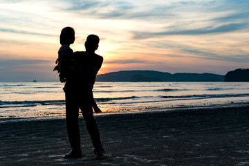 Father holding a daughter on the beach watching a tropical sunset