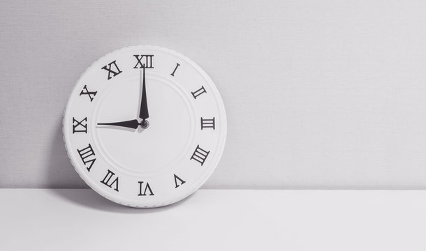 Closeup white clock for decorate in 9 o'clock on white wood desk and wallpaper textured background in black and white tone with copy space