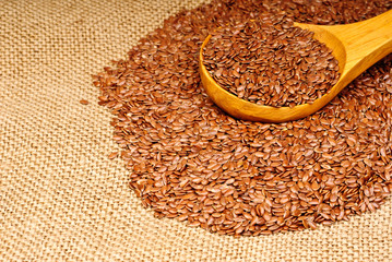 close up of flax seeds in wooden spoon on canvas  background