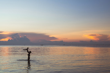Silhouette of mother with her baby against the sunset and lens flare at sea. Asian family activity lifestyle.