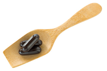 Top view of 3 dark black medicine soft gel capsules on wooden spoon isolated on white background