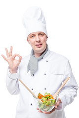 portrait of admiring chef with salad in hands showing hand gesture on a white background