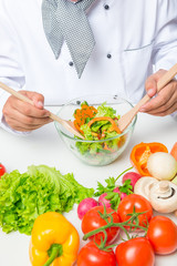 cook hands stirred of salad vegetables with two wooden spoons on a white table