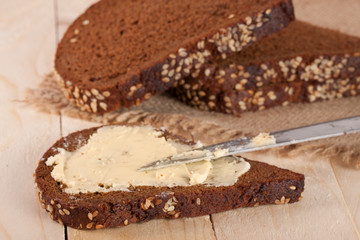 slices of black bread with sesame seeds and butter on a light wooden background