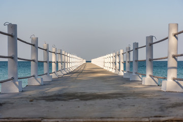 White posted concrete jetty leading out to a calm sea.