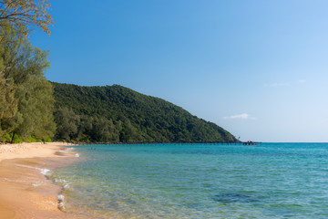 White sandy beach bay with wooden pier and forested headland in the distance on a tropical island.
