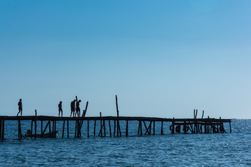 A silhouetted group of friends walk along an old wooden pier