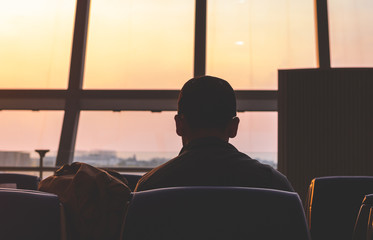 A man waring cap sitting and waiting for the flight in the airport, ready for departure,