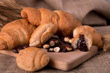 Chocolate croissants on board near wheat on wooden sackcloth background. Rustic style