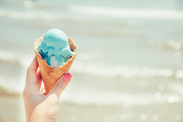 Woman's hand is holding ice cream on sea background. Summer. Vacation