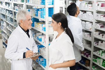 Chemist Looking At Coworker While Writing On Clipboard