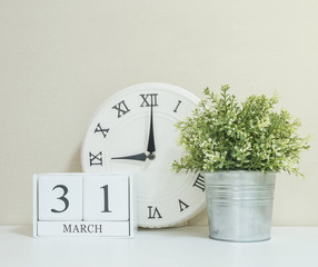 White wooden calendar with black 31 march word with clock and plant on white wood desk and cream...