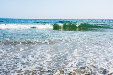 Sea tidal waves with white foam on a sunny sandy beach in resort on summer vacation. Background of ocean water texture