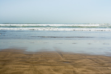 Sea tidal waves with white foam on a sunny sandy beach in resort on summer vacation. Background of ocean water texture