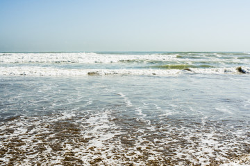 Sea tidal waves with white foam on a sunny sandy beach in resort on summer vacation. Background of ocean water texture