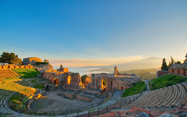 Ancient theatre of Taormina with Etna erupting volcano at sunset