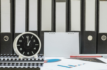 Closeup white clock for decorate in 1 o'clock desk of officer with work paper and document file in office room textured background in work concept