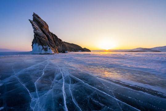 Lake Baikal during warm sunrise in winter. Beautiful rocks and crack lines on ice.