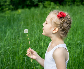 Young girl in the park blowing on dandelion