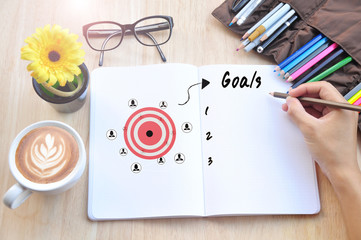hand writing goals memo list on a notebook with cup of coffee on wooden desk.