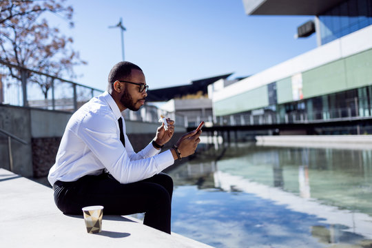 Elegant young man sitting on stairs drinking coffee and eating snack.