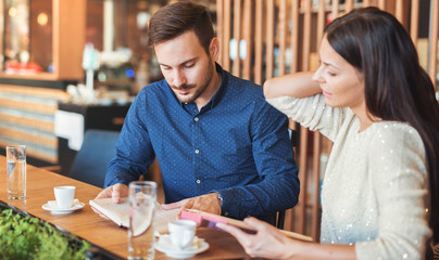 Young couple drinking coffee and reading a book in the cafe. Education, dating, relationships, love concept